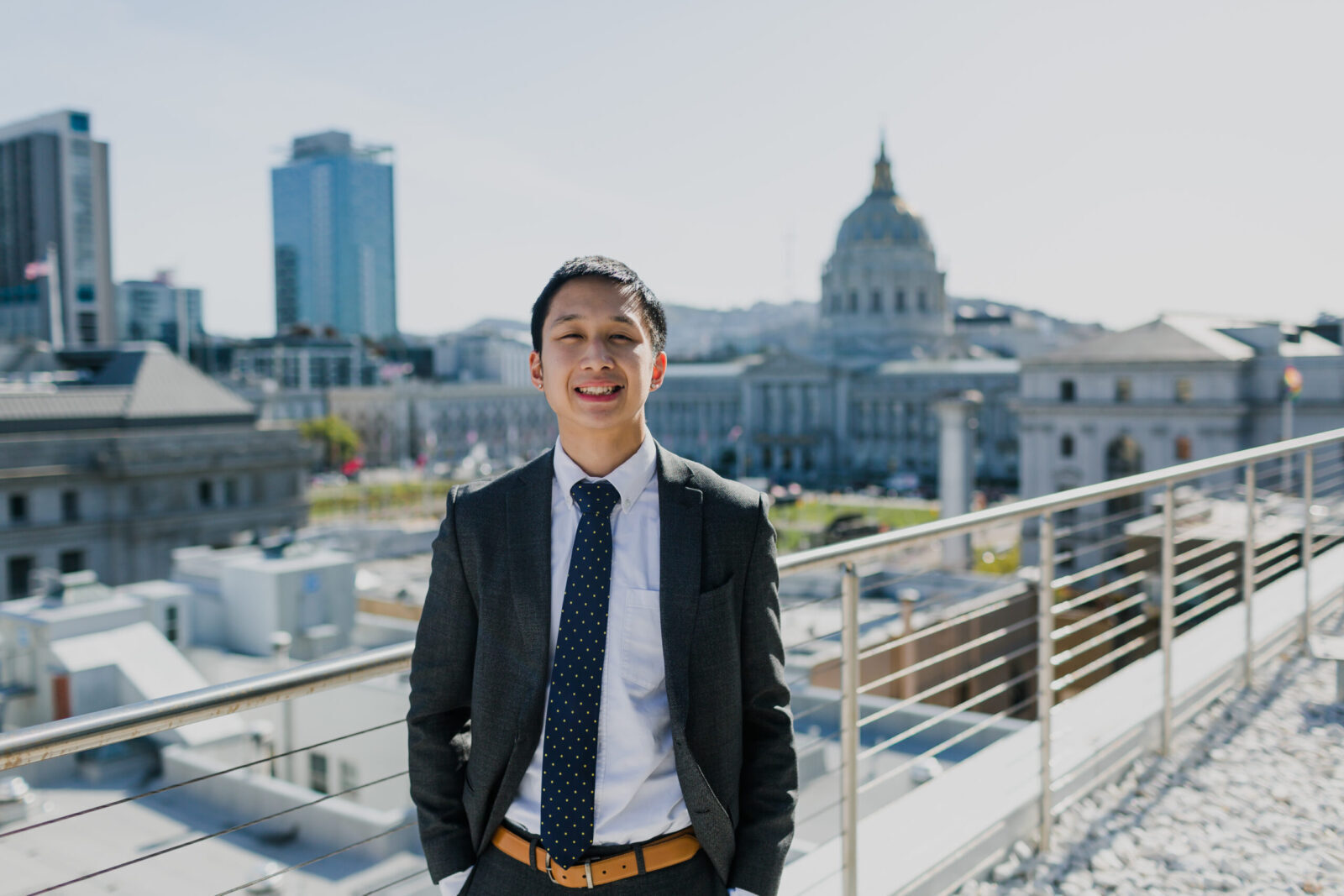 Ritchie Lee wearing a suit, smiling and posing at UC Law SF with San Francisco City Hall in the background