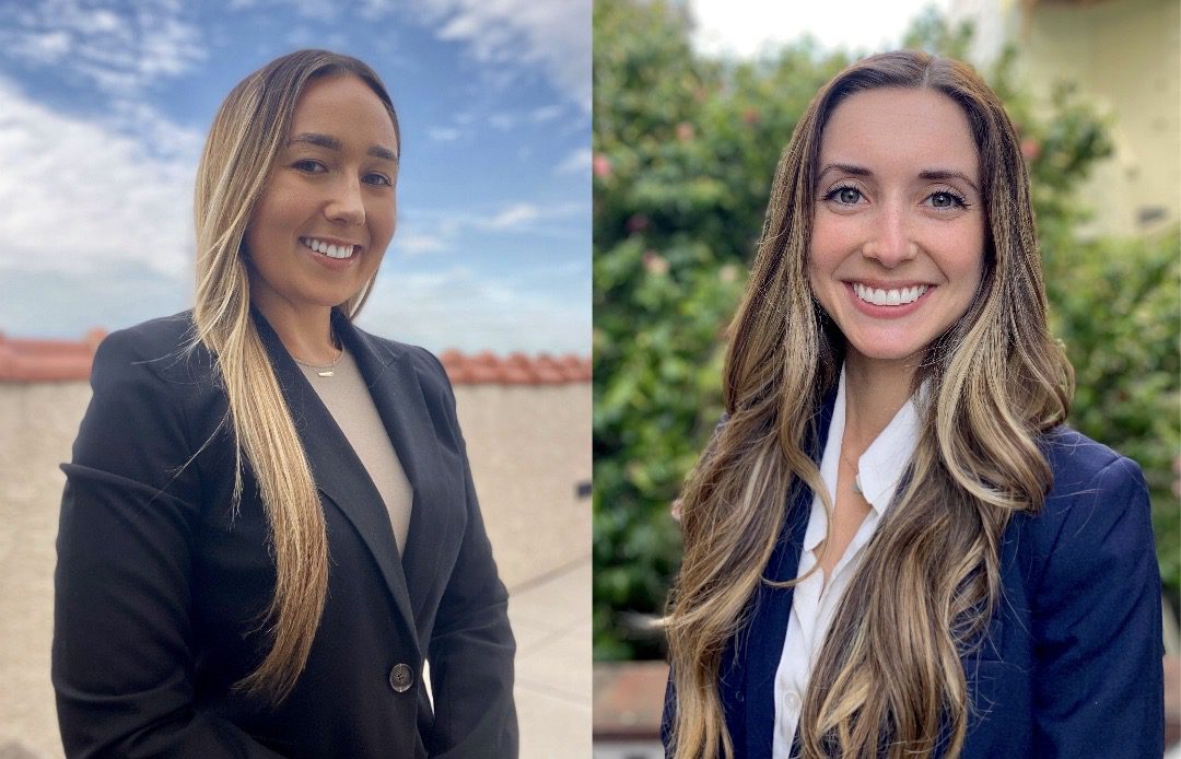 two smiling professional women in business suits standing outside