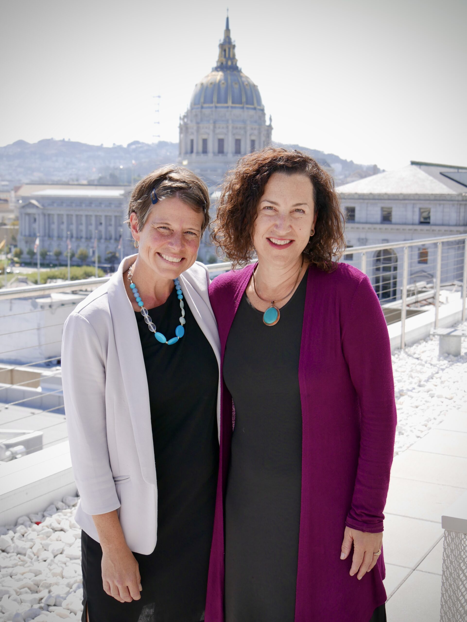 Two professional women stand in front of City Hall dome